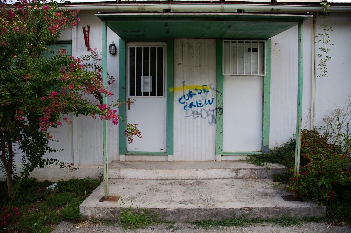 A white and green building with graffiti on the door

Description automatically generated